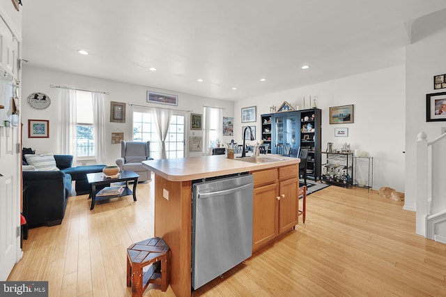 kitchen featuring stainless steel dishwasher, sink, a center island with sink, and light wood-type flooring