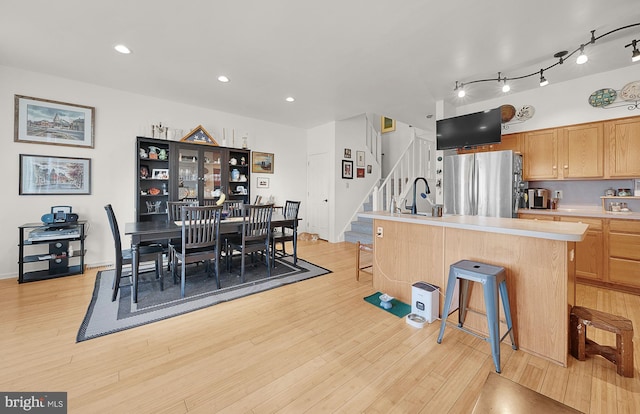 kitchen featuring sink, a breakfast bar area, stainless steel refrigerator, a center island with sink, and light wood-type flooring