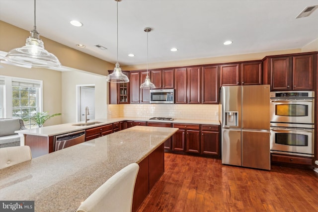 kitchen featuring decorative light fixtures, sink, backsplash, stainless steel appliances, and light stone countertops