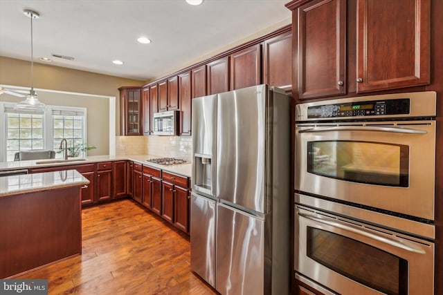 kitchen featuring appliances with stainless steel finishes, decorative light fixtures, sink, decorative backsplash, and light hardwood / wood-style flooring