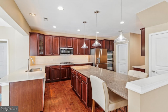 kitchen with appliances with stainless steel finishes, decorative light fixtures, sink, a kitchen bar, and decorative backsplash