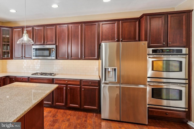 kitchen featuring dark hardwood / wood-style floors, pendant lighting, backsplash, light stone counters, and stainless steel appliances