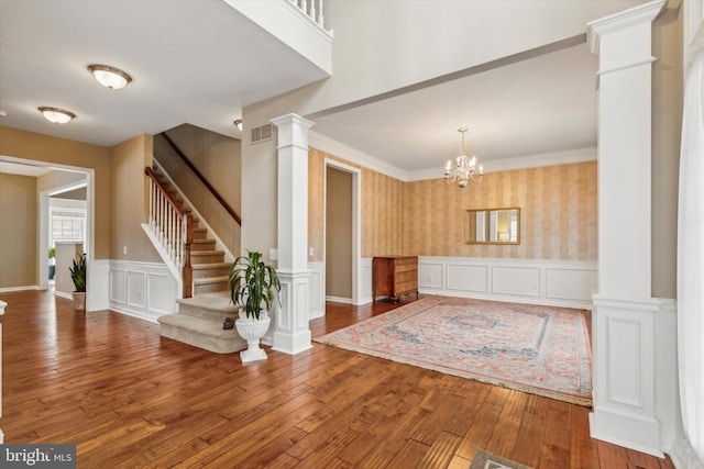 entryway featuring hardwood / wood-style flooring, an inviting chandelier, crown molding, and decorative columns