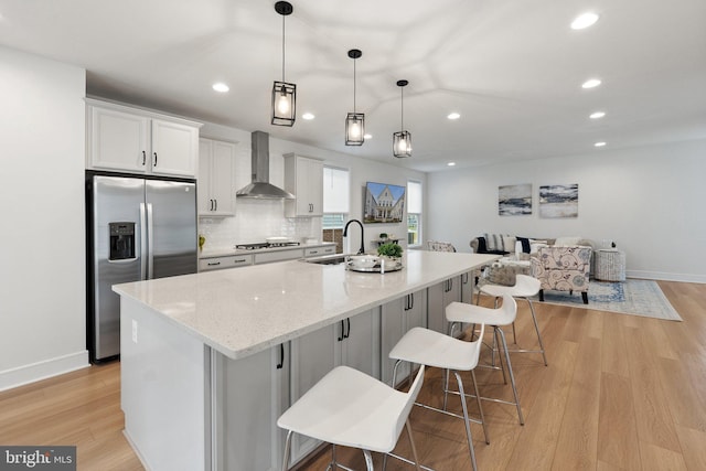 kitchen with sink, white cabinetry, stainless steel appliances, a kitchen breakfast bar, and wall chimney exhaust hood