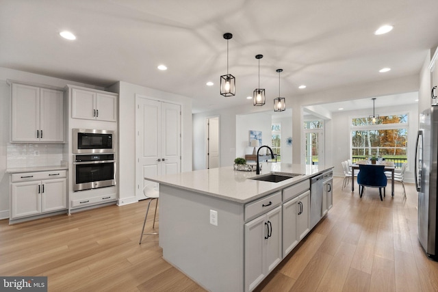 kitchen featuring sink, a kitchen island with sink, white cabinetry, hanging light fixtures, and stainless steel appliances