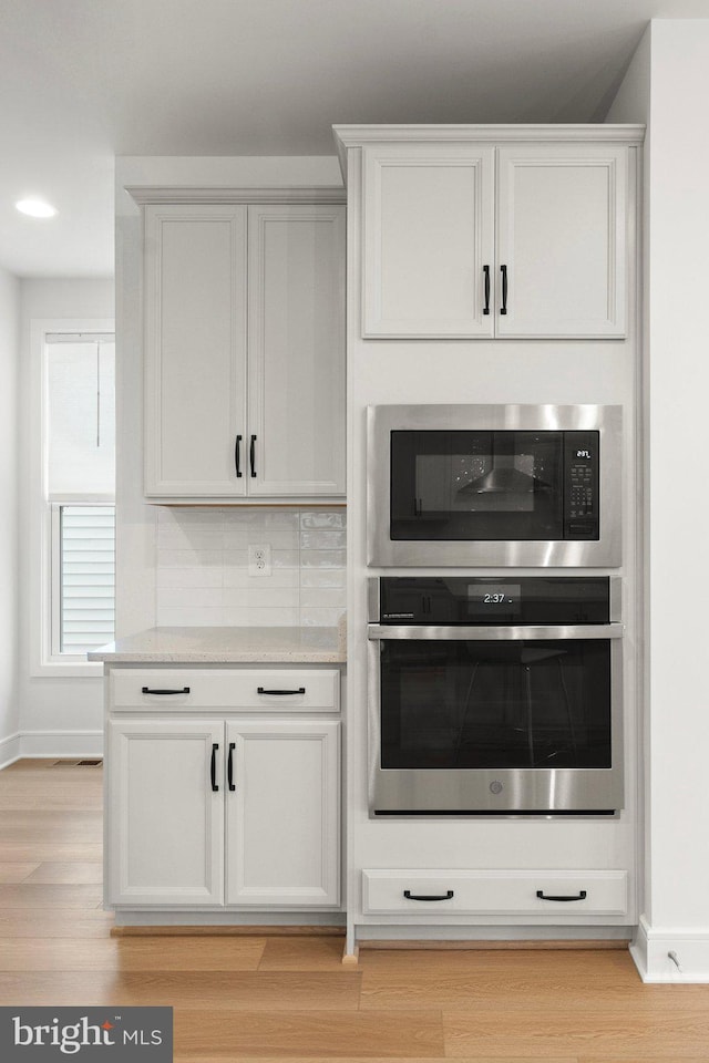 kitchen with white cabinetry, decorative backsplash, appliances with stainless steel finishes, and light hardwood / wood-style flooring