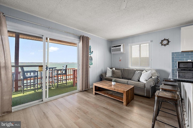 living room featuring light hardwood / wood-style flooring, an AC wall unit, a textured ceiling, and a water view