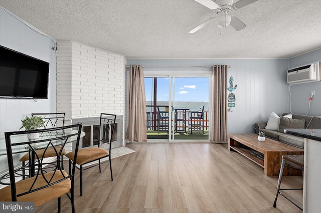 living room with a textured ceiling, a wall unit AC, ceiling fan, and light wood-type flooring