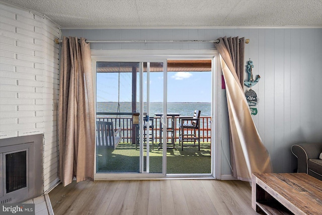 doorway to outside with hardwood / wood-style flooring, a fireplace, a textured ceiling, and a water view