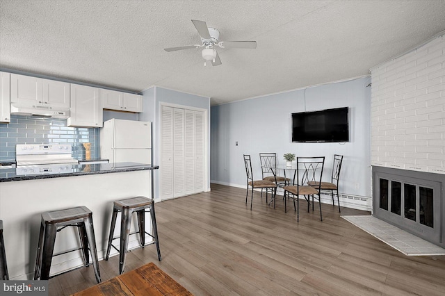 kitchen featuring a breakfast bar, hardwood / wood-style floors, a fireplace, white cabinetry, and white appliances