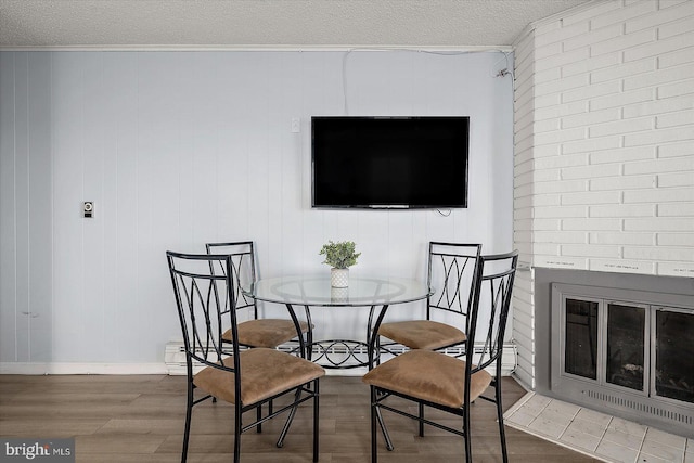 dining space with ornamental molding, a brick fireplace, hardwood / wood-style floors, and a textured ceiling