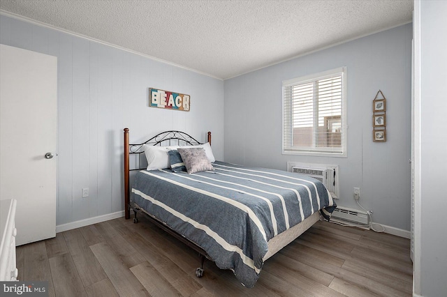 bedroom with a baseboard heating unit, light hardwood / wood-style floors, a textured ceiling, and an AC wall unit