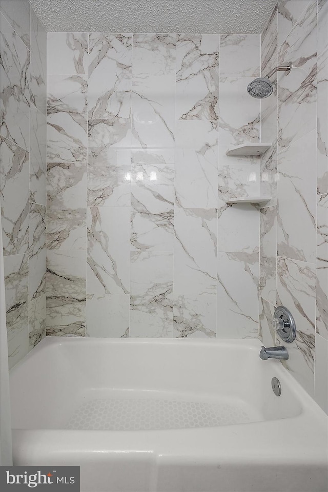 bathroom with tiled shower / bath combo and a textured ceiling