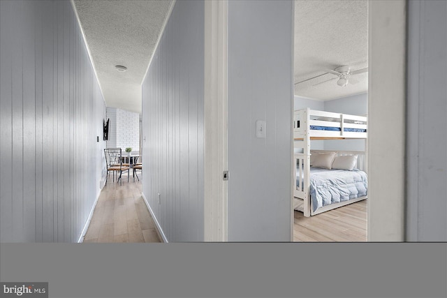 hallway featuring wood walls, light hardwood / wood-style flooring, and a textured ceiling