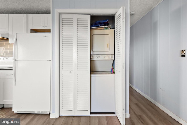 washroom with stacked washer / dryer, light hardwood / wood-style flooring, and a textured ceiling