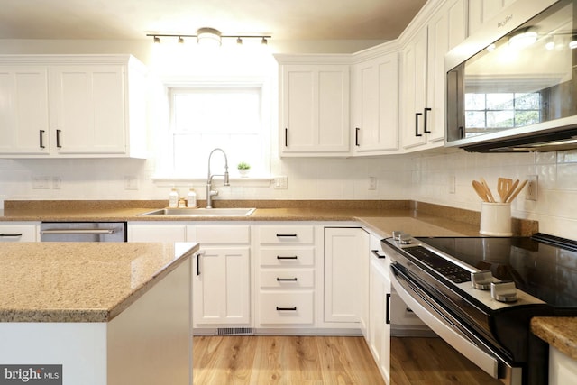 kitchen featuring sink, appliances with stainless steel finishes, white cabinetry, backsplash, and light stone counters