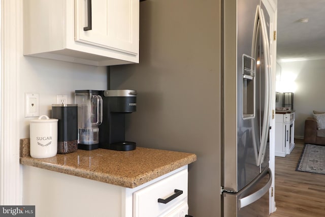 kitchen with stainless steel refrigerator with ice dispenser, light stone countertops, hardwood / wood-style floors, and white cabinets