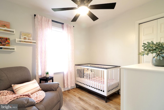 bedroom with multiple windows, a nursery area, ceiling fan, and light hardwood / wood-style flooring