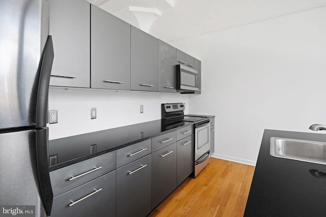 kitchen with sink, light hardwood / wood-style flooring, gray cabinets, and appliances with stainless steel finishes