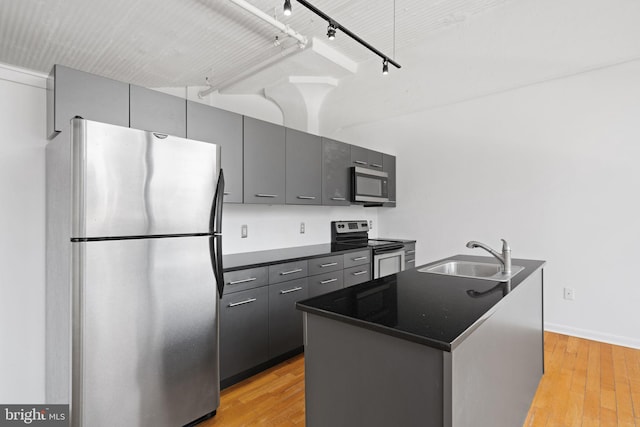 kitchen featuring stainless steel appliances, a kitchen island with sink, sink, and light wood-type flooring