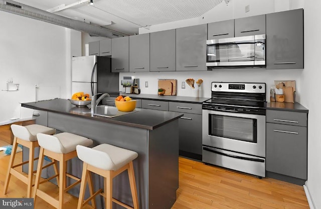 kitchen with appliances with stainless steel finishes, a breakfast bar, and gray cabinetry
