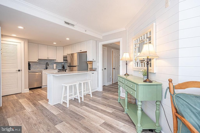 kitchen with appliances with stainless steel finishes, white cabinets, a kitchen bar, kitchen peninsula, and light hardwood / wood-style flooring