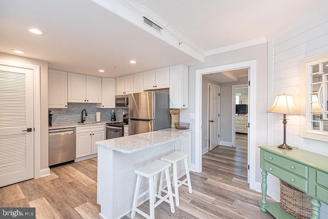 kitchen with a breakfast bar, light stone counters, crown molding, appliances with stainless steel finishes, and white cabinets