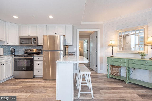 kitchen with appliances with stainless steel finishes, light hardwood / wood-style floors, a breakfast bar area, and white cabinets