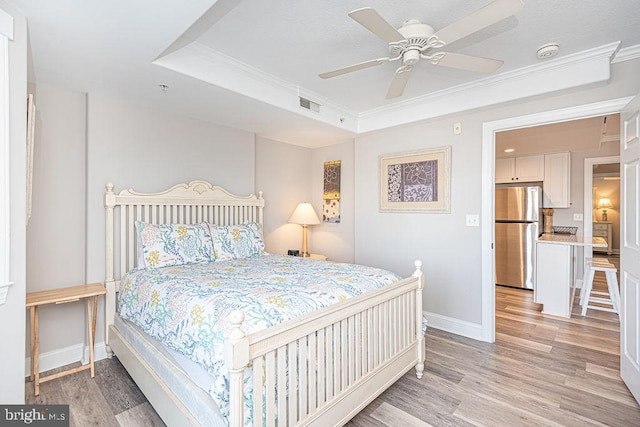 bedroom featuring crown molding, stainless steel refrigerator, a raised ceiling, and light wood-type flooring