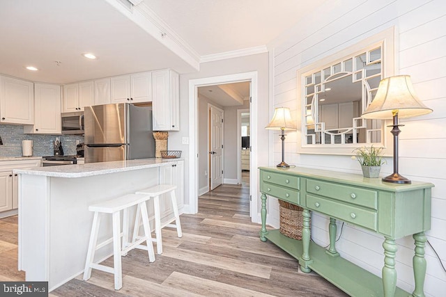 kitchen with stainless steel appliances, tasteful backsplash, ornamental molding, white cabinets, and light wood-type flooring