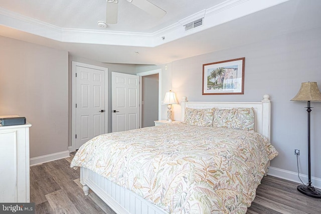 bedroom with wood-type flooring, ornamental molding, ceiling fan, a tray ceiling, and a closet