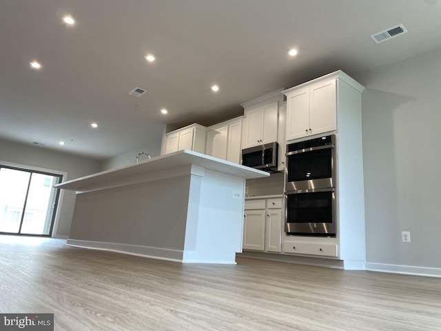 kitchen with light hardwood / wood-style floors, white cabinets, and appliances with stainless steel finishes