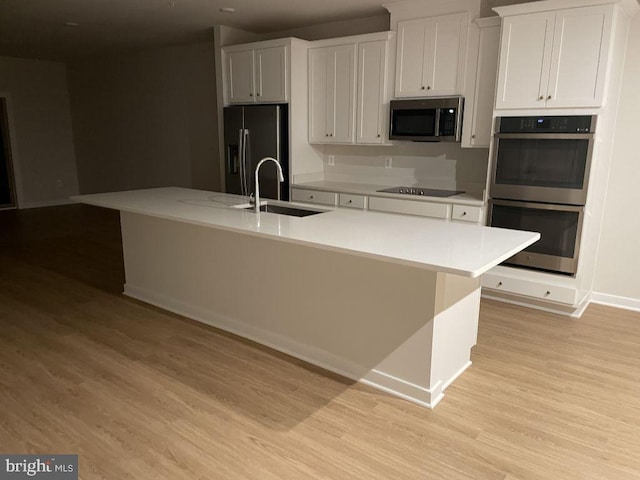 kitchen featuring a center island with sink, appliances with stainless steel finishes, light countertops, and a sink