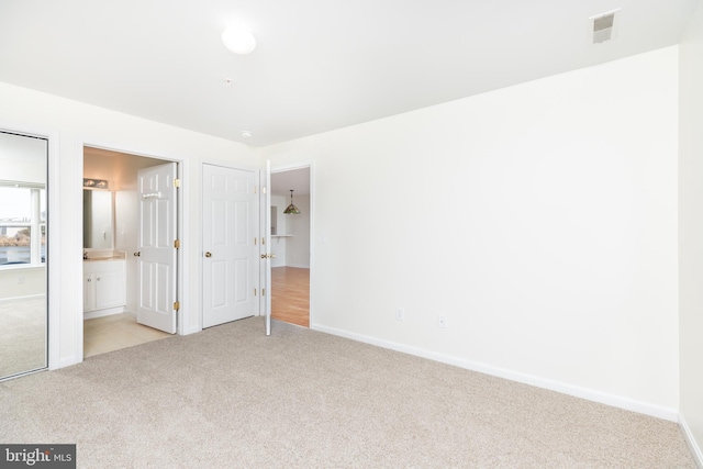 unfurnished bedroom featuring light colored carpet and ensuite bath