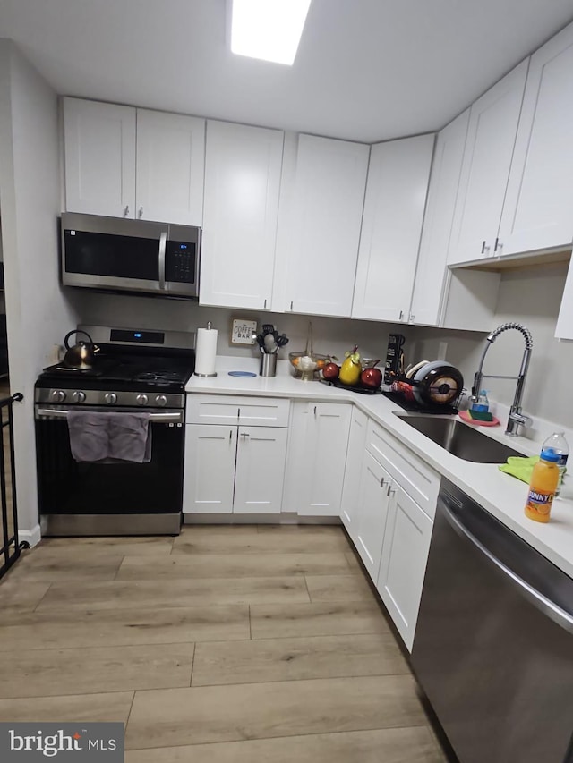 kitchen featuring stainless steel appliances, sink, light hardwood / wood-style flooring, and white cabinets