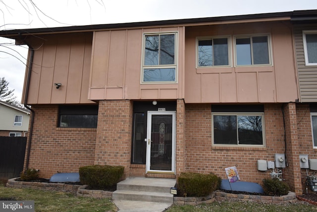 view of front of home featuring board and batten siding, fence, and brick siding