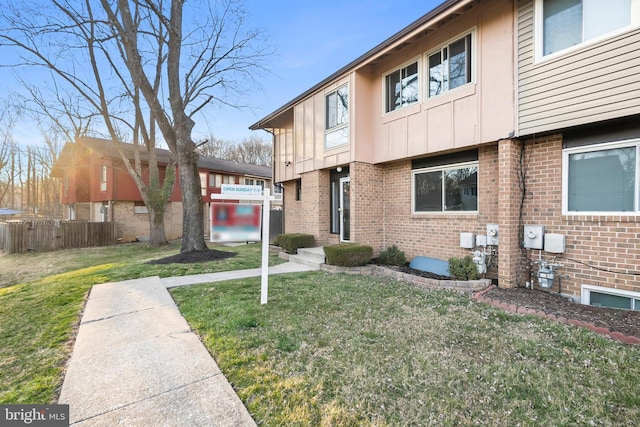 exterior space featuring brick siding, board and batten siding, a front yard, and fence