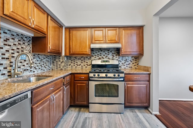 kitchen featuring light wood-type flooring, a sink, stainless steel appliances, under cabinet range hood, and tasteful backsplash