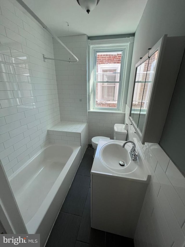 full bathroom with tile walls, vanity, tiled shower / bath combo, and toilet