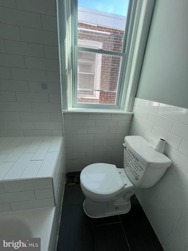 bathroom featuring tile walls, toilet, and a healthy amount of sunlight