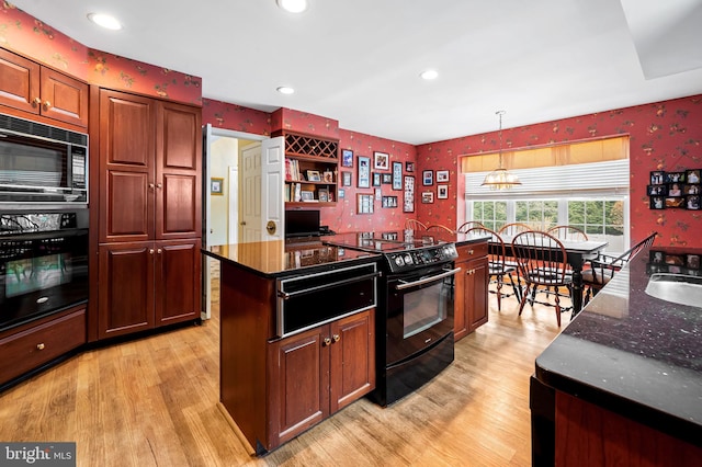 kitchen with light wood-type flooring, a kitchen island, black appliances, and decorative light fixtures