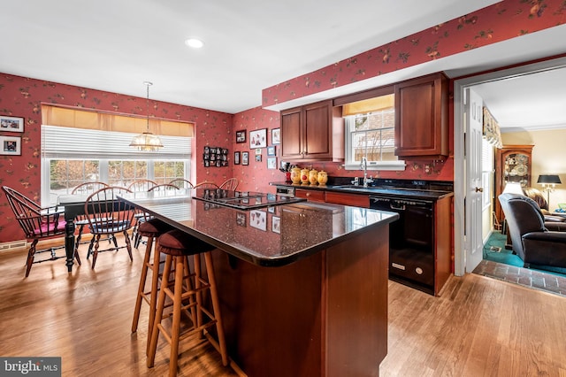 kitchen featuring a center island, a breakfast bar, light hardwood / wood-style flooring, decorative light fixtures, and black appliances