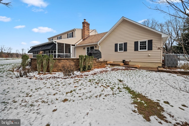 snow covered rear of property with a sunroom