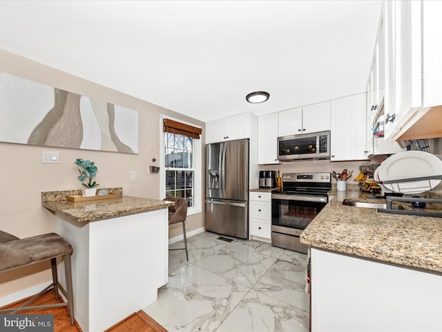 kitchen featuring a breakfast bar area, light stone counters, appliances with stainless steel finishes, kitchen peninsula, and white cabinets