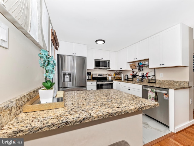 kitchen featuring white cabinetry, light stone countertops, stainless steel appliances, and kitchen peninsula