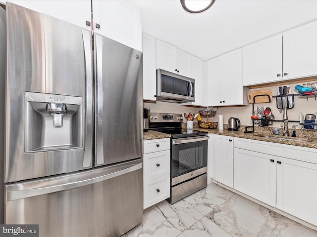 kitchen featuring appliances with stainless steel finishes, sink, dark stone countertops, and white cabinets