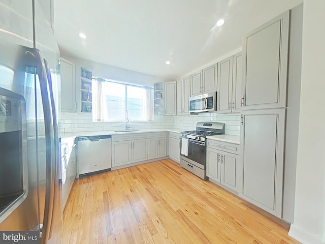 kitchen with tasteful backsplash, stainless steel appliances, sink, and light wood-type flooring