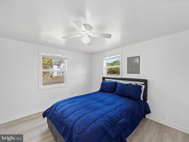 bedroom with a ceiling fan, electric panel, light wood-style flooring, and baseboards