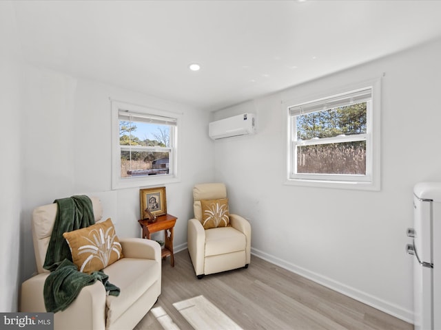 living area featuring a healthy amount of sunlight, light wood-style flooring, baseboards, and a wall mounted air conditioner