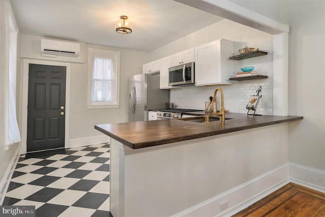 kitchen featuring appliances with stainless steel finishes, backsplash, a wall mounted AC, white cabinets, and kitchen peninsula